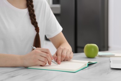 Woman writing in notebook at white marble table indoors, closeup