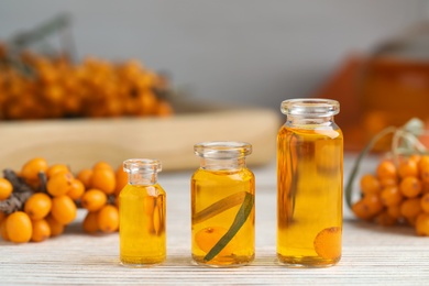 Photo of Natural sea buckthorn oil and fresh berries on white wooden table