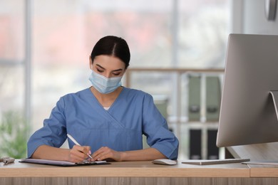 Photo of Receptionist with protective mask working at countertop in hospital