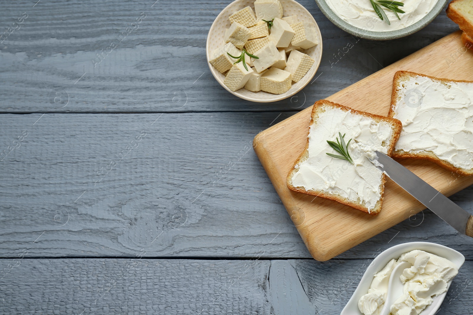 Photo of Delicious toasts with tofu cream cheese and rosemary on grey wooden table, flat lay. Space for text