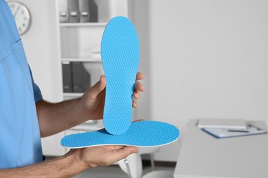 Male orthopedist showing insoles in hospital, closeup