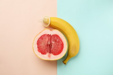 Photo of Banana with condom and half of grapefruit on color background, flat lay. Safe sex concept