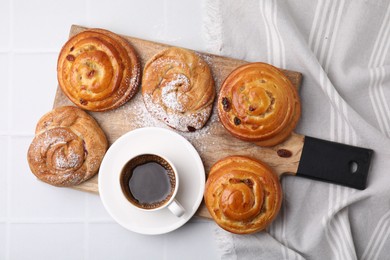 Photo of Delicious rolls with raisins, powdered sugar and coffee cup on white tiled table, top view. Sweet buns