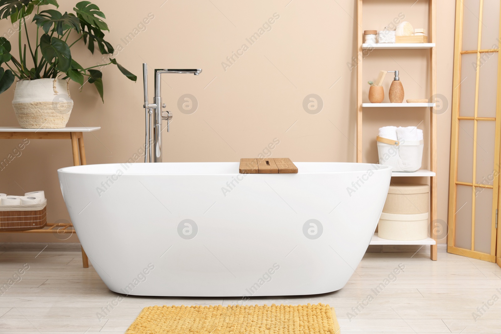 Photo of Bath tub with wooden board and different personal care products and accessories on shelving unit in bathroom