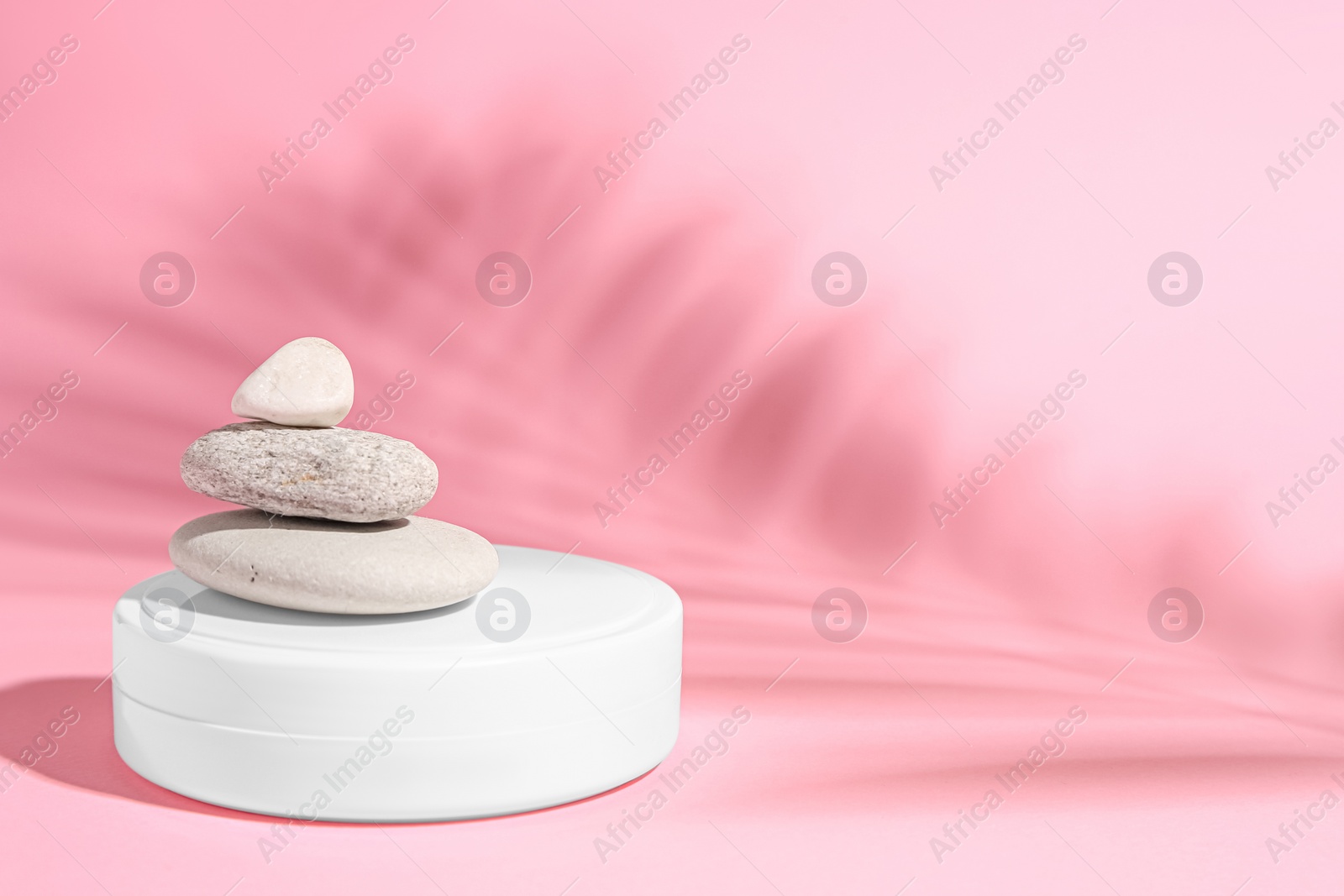 Photo of Cosmetic product, stacked stones and shadow of tropical leaf on pink background. Space for text