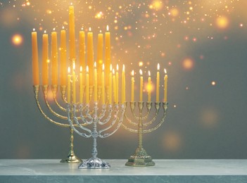 Image of Hanukkah celebration. Menorahs with burning candles on grey marble table, space for text