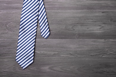 Photo of Stylish striped silk necktie on dark grey wooden table, top view with space for text