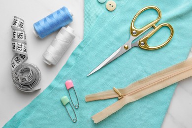 Threads and other sewing supplies on white marble table, flat lay