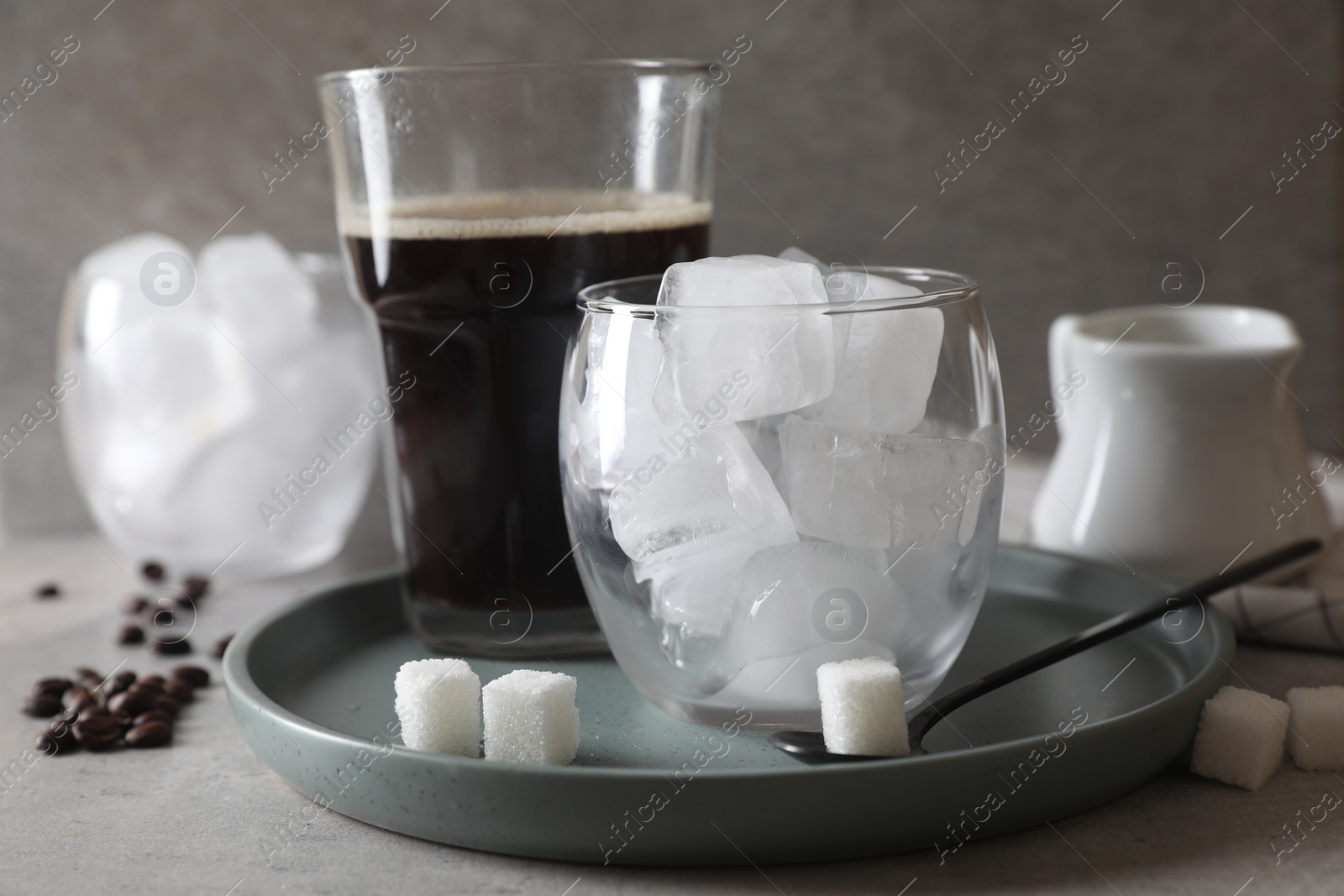 Photo of Making iced coffee. Ice cubes in glass, ingredients and spoon on gray table, closeup