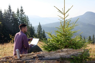 Photo of Man working on laptop outdoors surrounded by beautiful nature