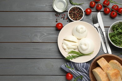 Photo of Delicious burrata cheese with arugula served on grey wooden table, flat lay. Space for text