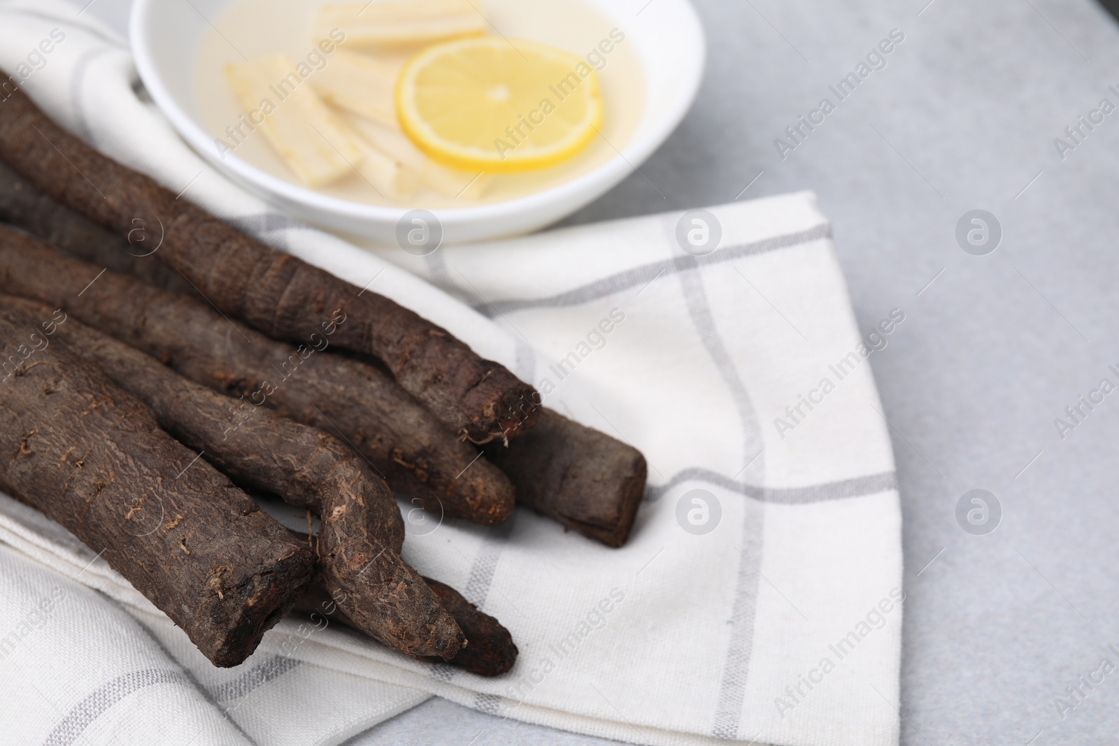 Photo of Raw salsify roots and bowl with lemon on white table, closeup. Space for text