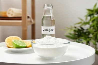 Photo of Bowl with baking soda, lemons and bottle of vinegar on table indoors