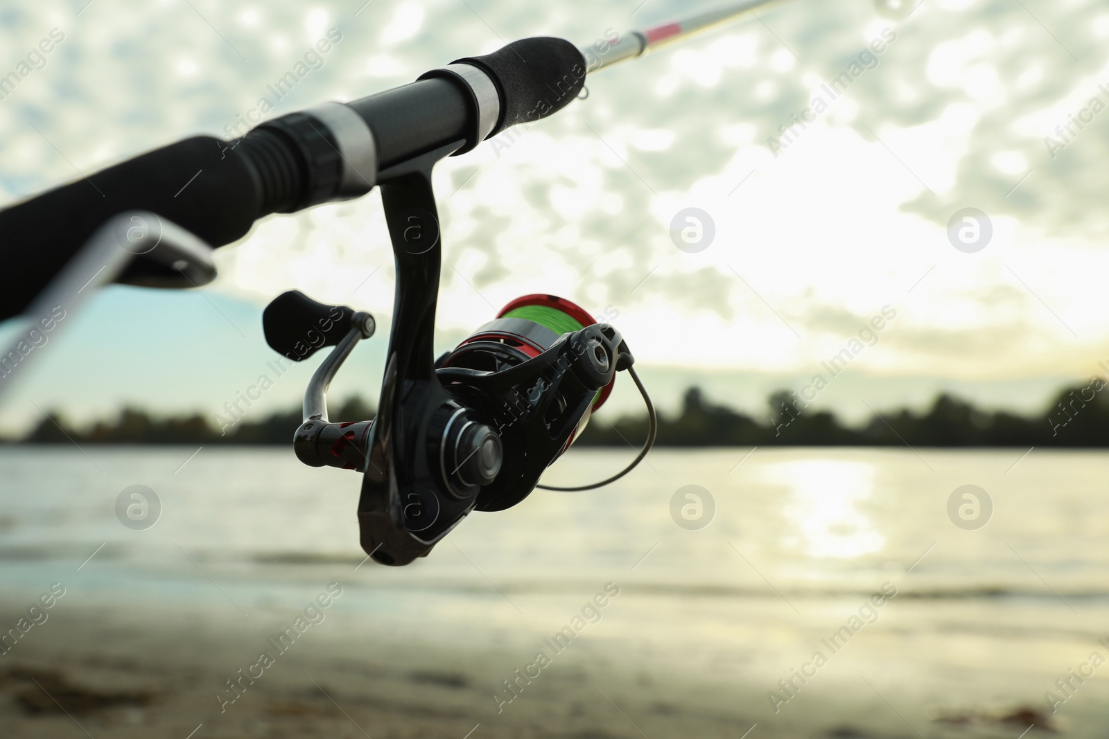 Photo of Fishing rod with reel near river, closeup. Space for text