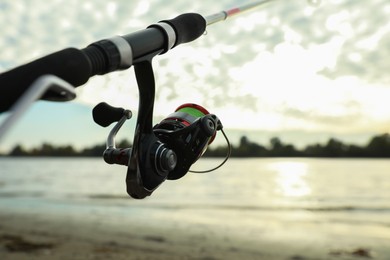 Fishing rod with reel near river, closeup. Space for text