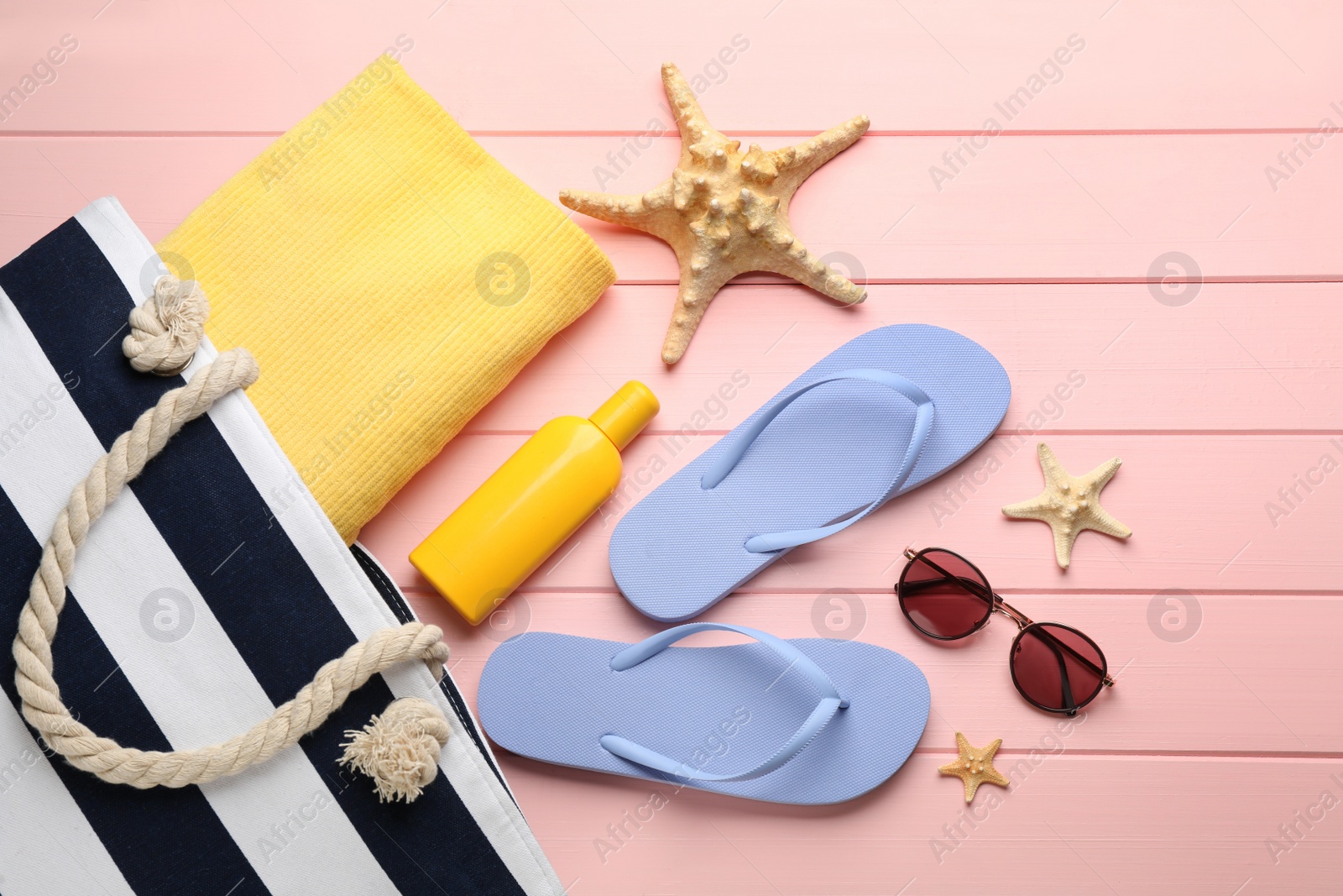 Photo of Stylish bag and beach accessories on pink wooden background, flat lay