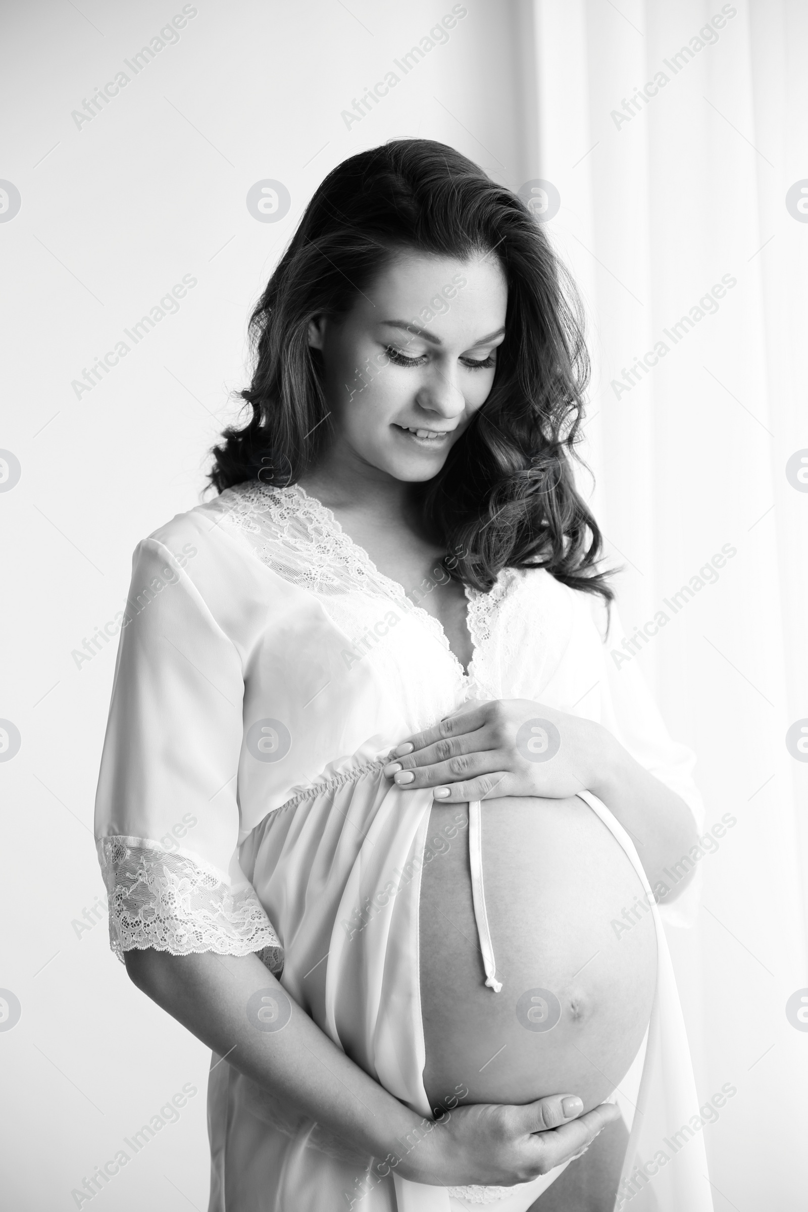 Photo of Young pregnant woman in lace nightgown on light background, black and white effect