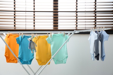 Photo of Different cute baby onesies hanging on clothes line indoors. Laundry day