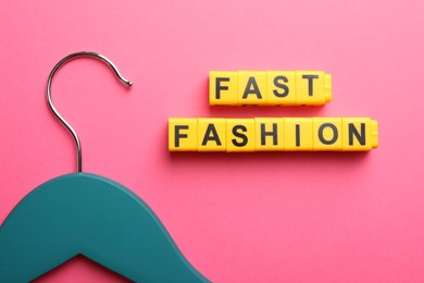 Photo of Yellow plastic cubes with phrase Fast Fashion and hanger on pink background, flat lay