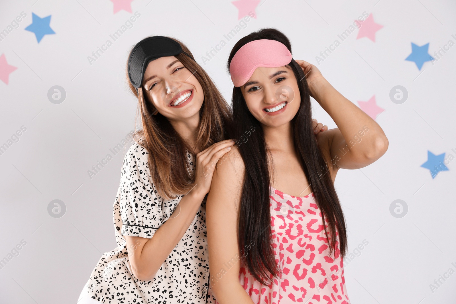 Photo of Beautiful women wearing sleeping masks on light grey background. Bedtime