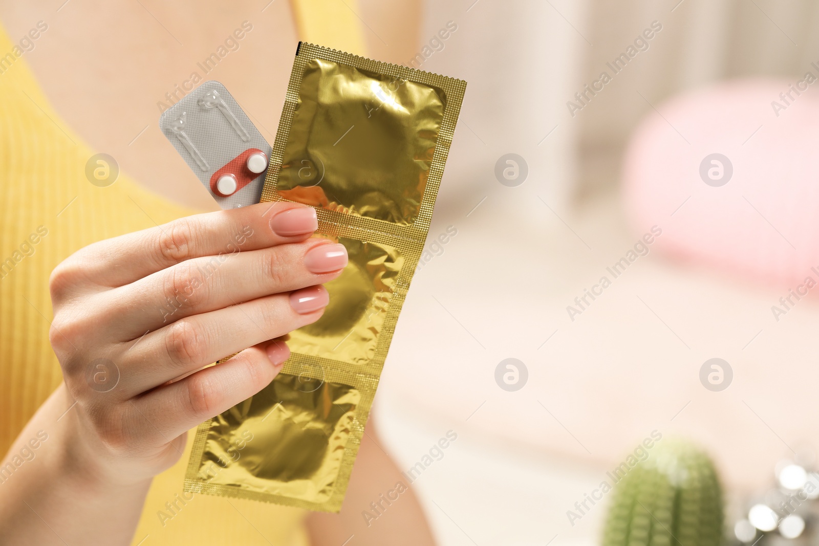 Photo of Woman holding condoms and contraceptive pills on blurred background, closeup with space for text. Choosing birth control method