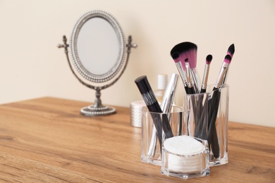 Organizer with cosmetic products for makeup and mirror on table against light wall