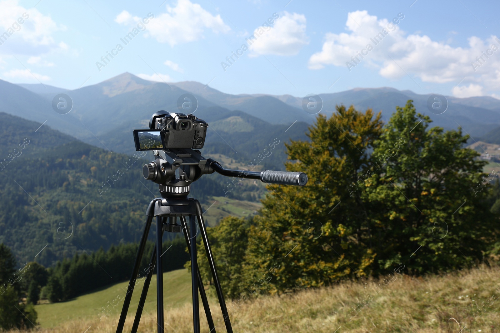 Photo of Tripod with modern camera in mountains on sunny day. Space for text