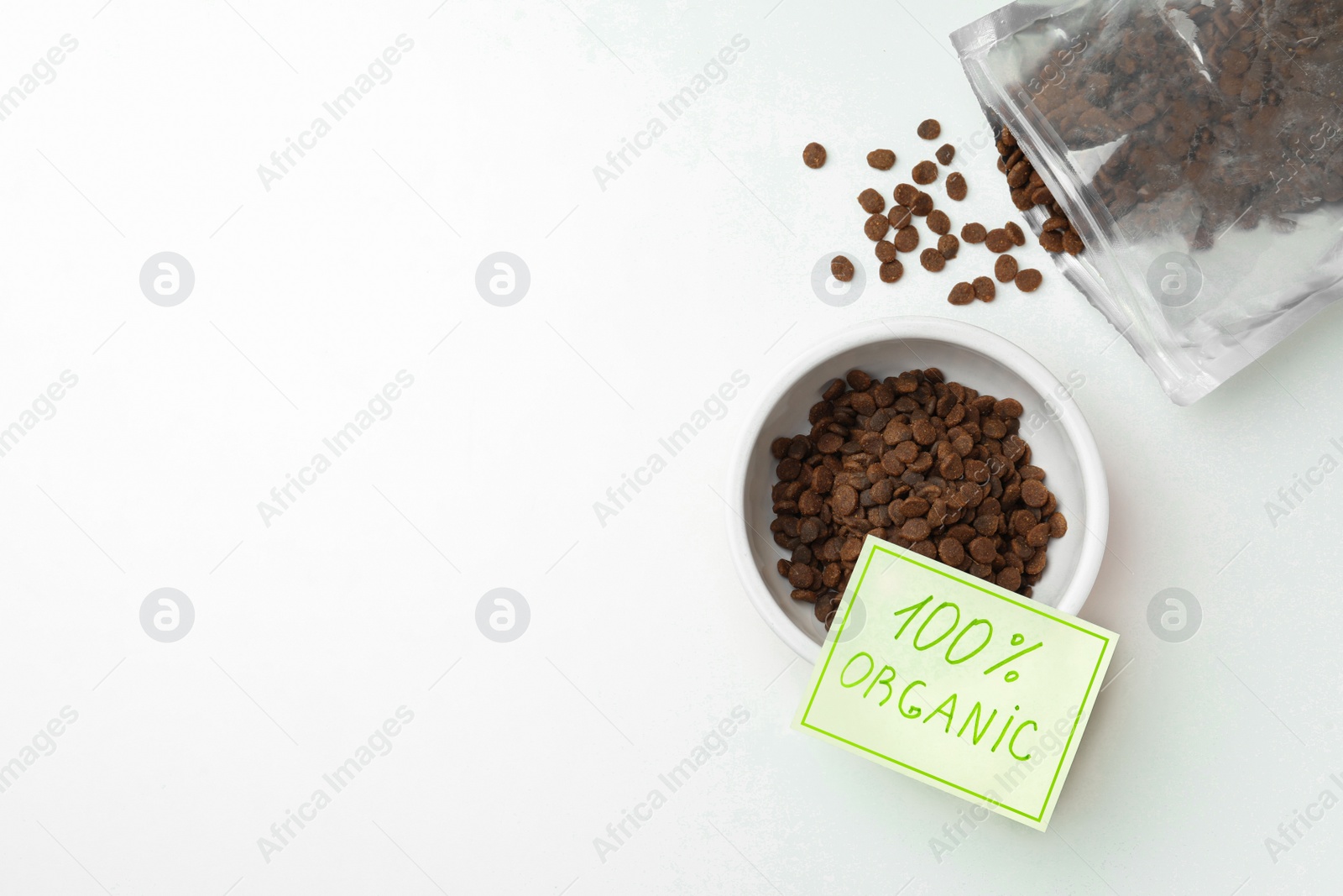 Photo of Pack and feeding bowl of dry cat food with note 100% Organic on white table, flat lay. Space for text