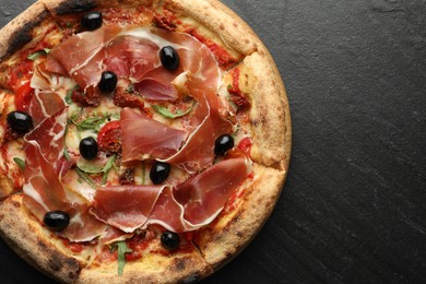 Tasty pizza with cured ham, olives and sun-dried tomato on black table, top view. Space for text