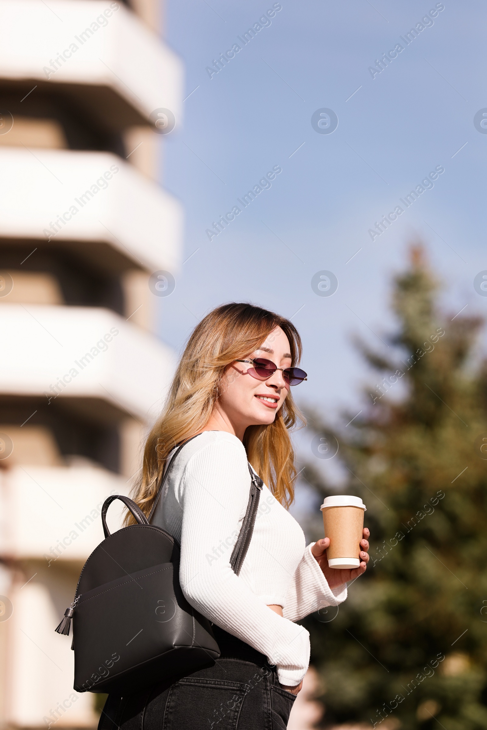 Photo of Young woman with stylish backpack and hot drink on autumn day