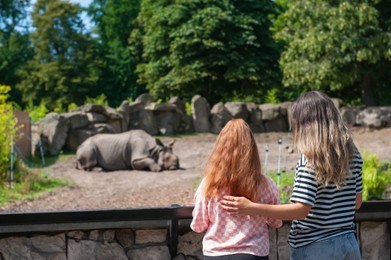 Woman with her daughter looking at wild rhinoceros in zoo