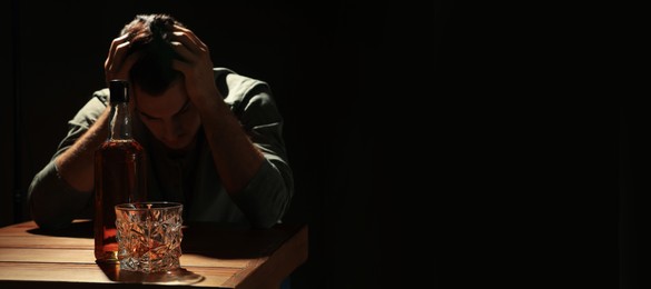 Image of Suffering from hangover. Man with alcoholic drink at table against black background, selective focus. Banner design with space for text