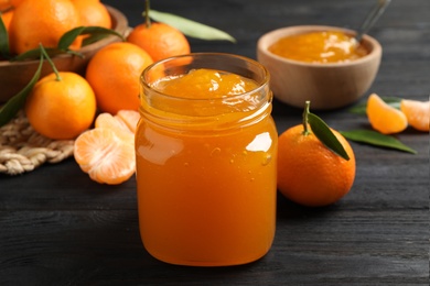 Photo of Tasty tangerine jam in glass jar on dark wooden table