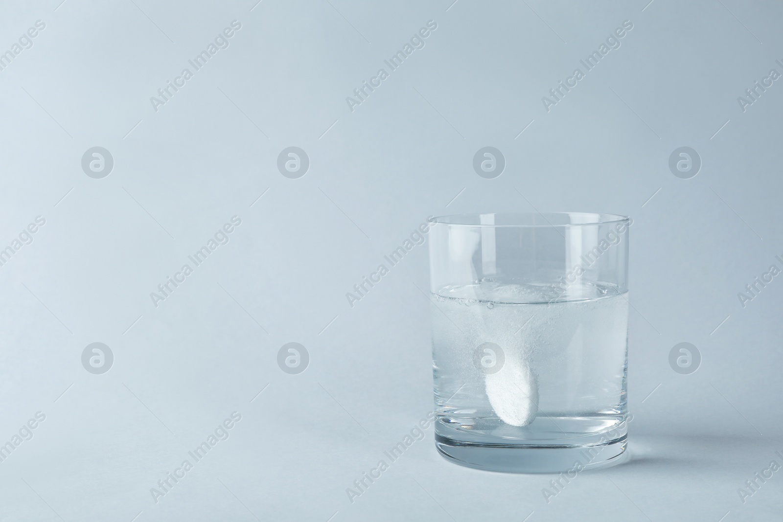 Photo of Glass of water with effervescent tablet on light grey background, space for text