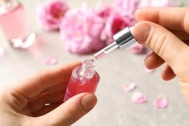 Photo of Woman dripping rose essential oil into bottle over table, closeup