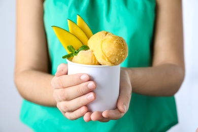 Photo of Woman holding bowl full of delicious ice cream and mango slices on light grey background, closeup