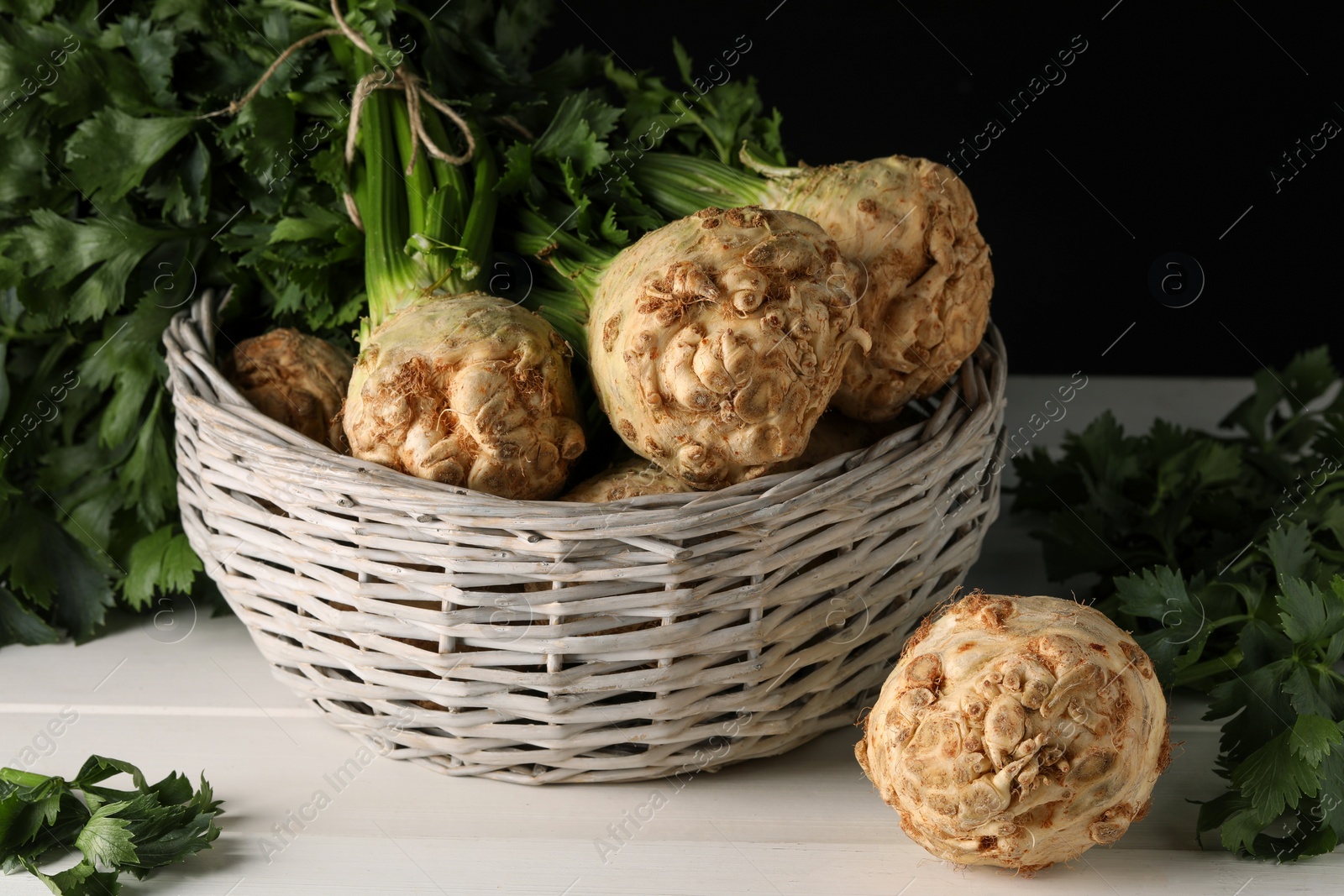 Photo of Fresh raw celery roots in wicker basket on white wooden table