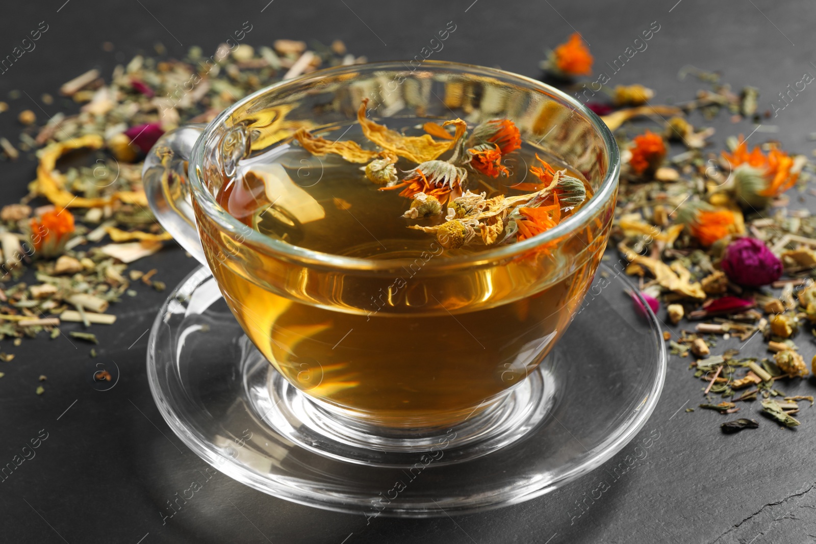 Photo of Freshly brewed tea and dried herbs on black table, closeup