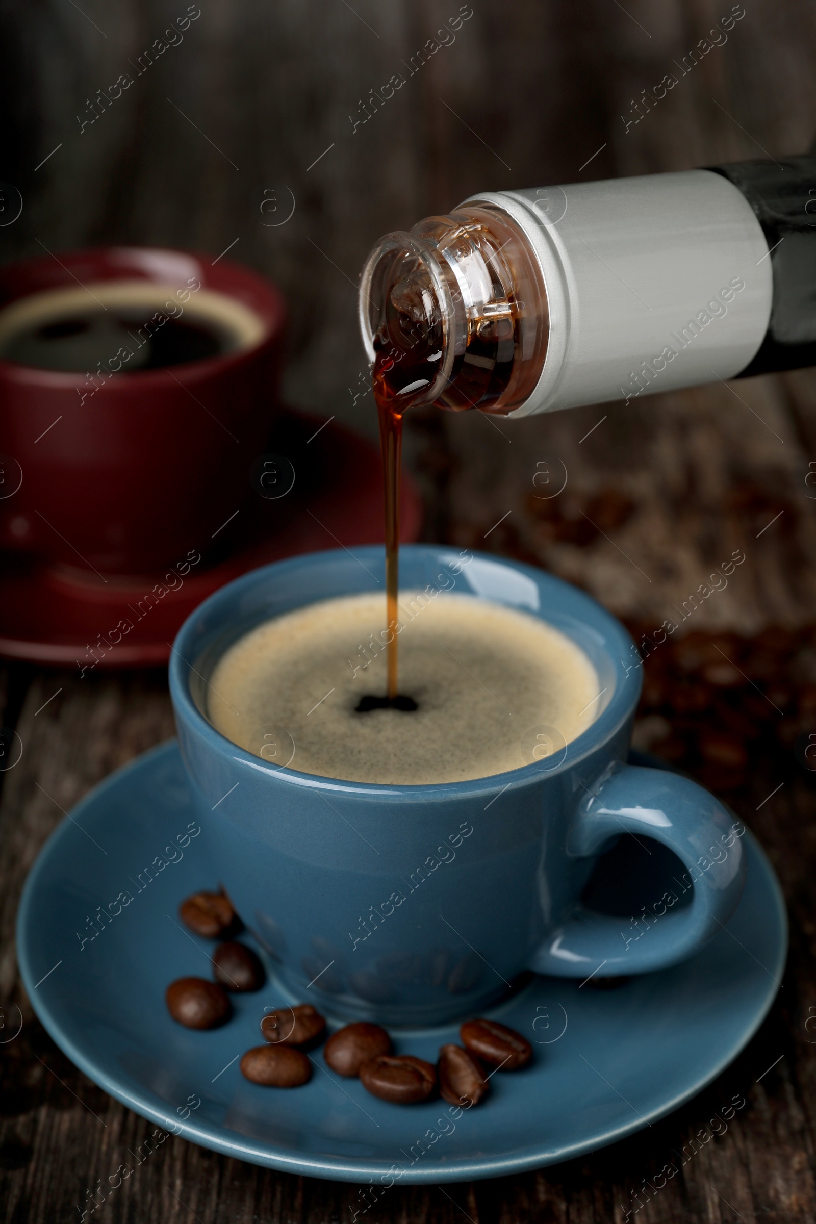 Photo of Pouring delicious syrup into cup with coffee at wooden table, closeup