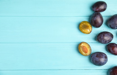 Delicious ripe plums on light blue wooden table, flat lay. Space for text