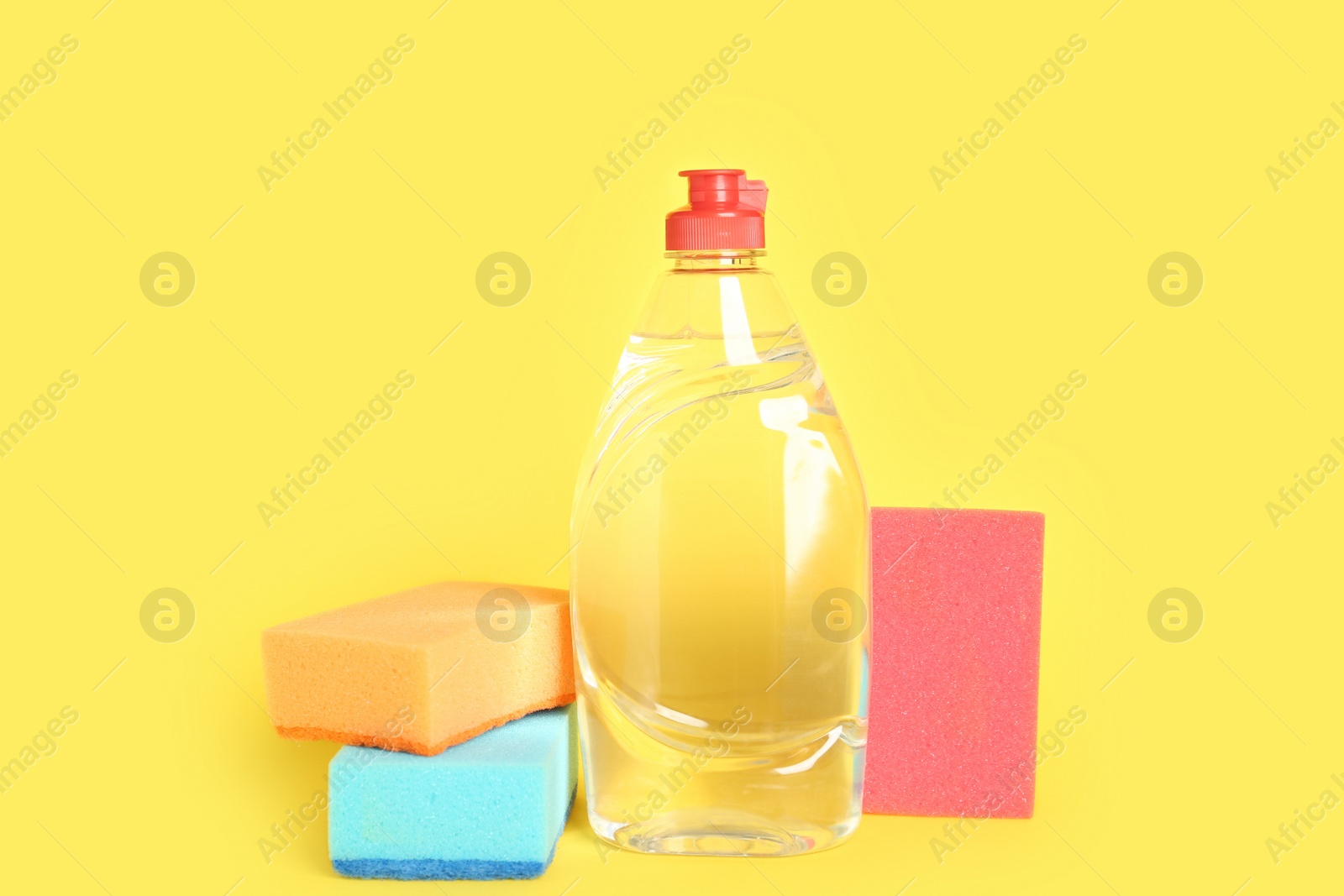 Photo of Bottle of detergent and sponges on yellow background