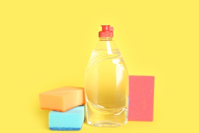 Photo of Bottle of detergent and sponges on yellow background