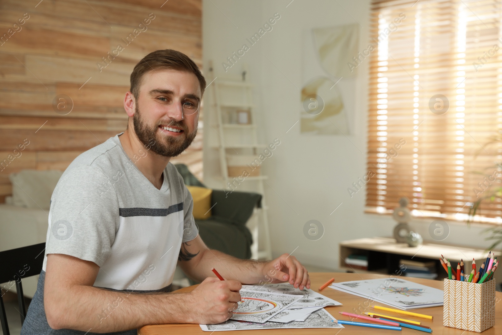 Photo of Young man coloring antistress picture at table indoors