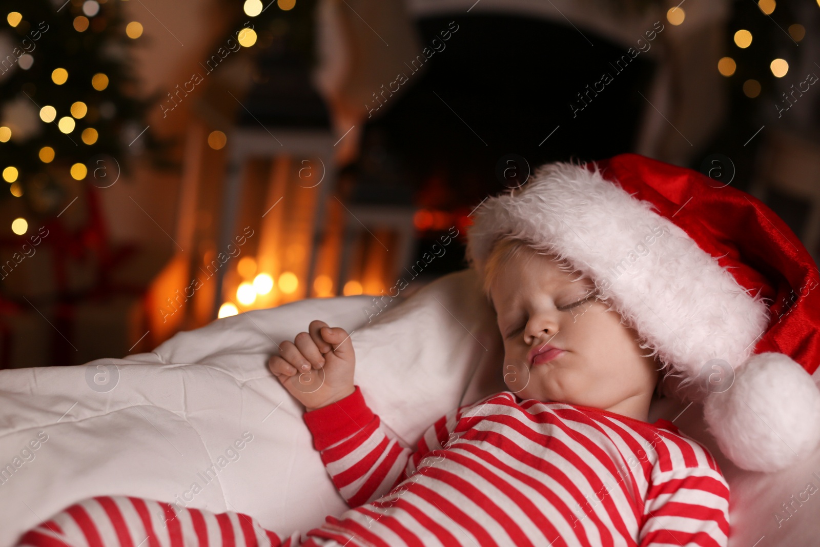 Photo of Baby in Christmas pajamas and Santa hat sleeping on bed indoors. Space for text