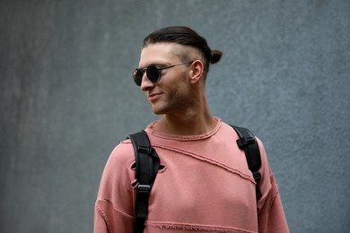 Photo of Handsome young man in stylish sunglasses and backpack near grey wall