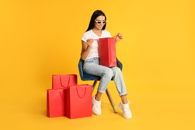 Beautiful young woman with paper shopping bags in armchair on yellow background