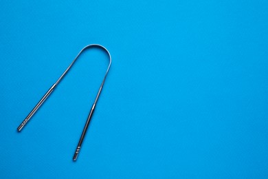 Photo of One tongue cleaner on blue background, top view with space for text. Dental care