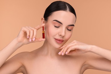 Beautiful young woman holding skincare ampoule on beige background