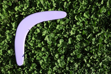 Photo of Violet wooden boomerang on green grass outdoors, above view. Space for text