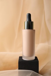 Photo of Bottle of skin foundation on beige tulle fabric. Makeup product